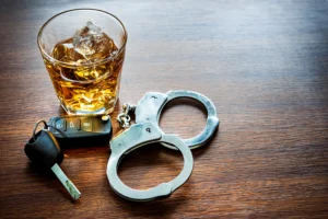 A glass of whiskey, car keys, and handcuffs on a table